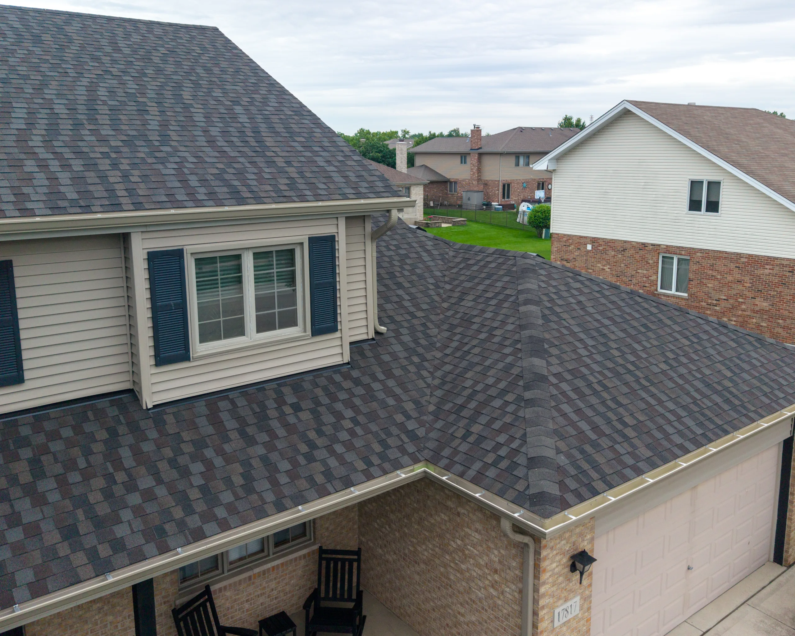 Elevated view of dimensional asphalt shingles on a two-story home with tan siding and a covered front porch