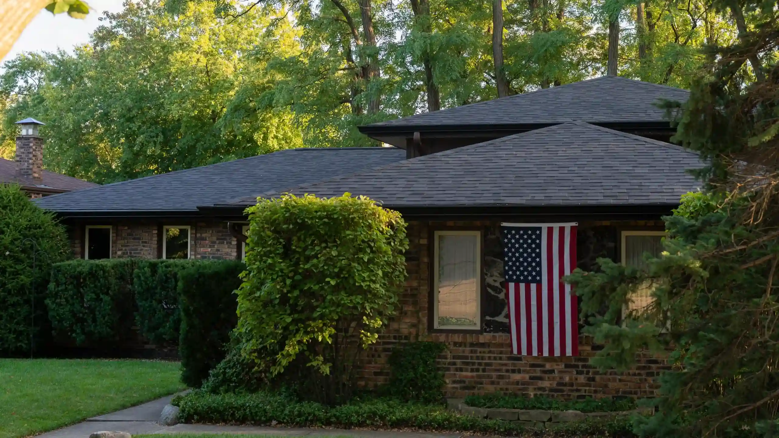 Brick ranch home with a new dark asphalt shingle roof and an American flag by the window