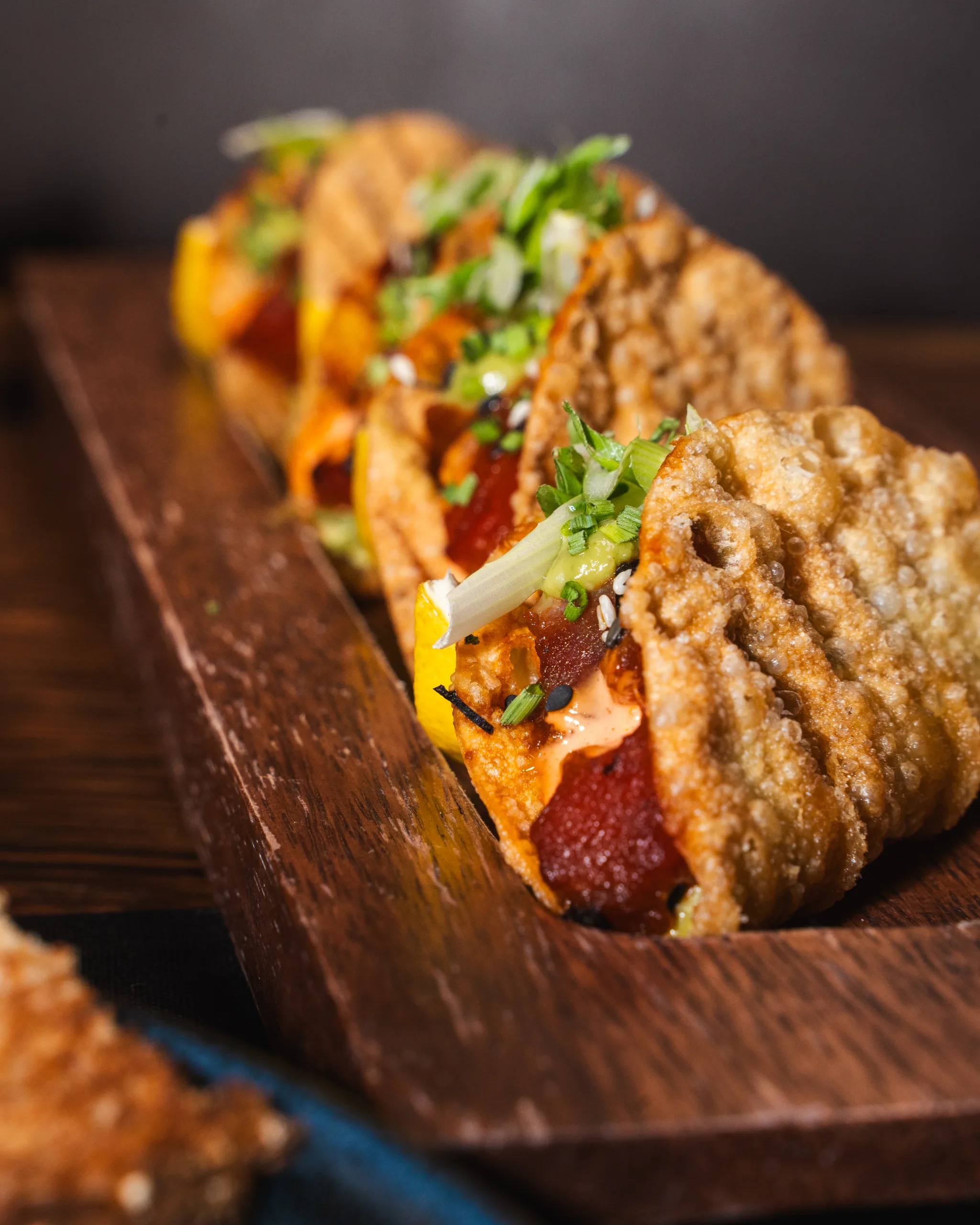 Crispy wonton tacos filled with tuna, spicy mayo, and green onion lined up on a wooden serving board