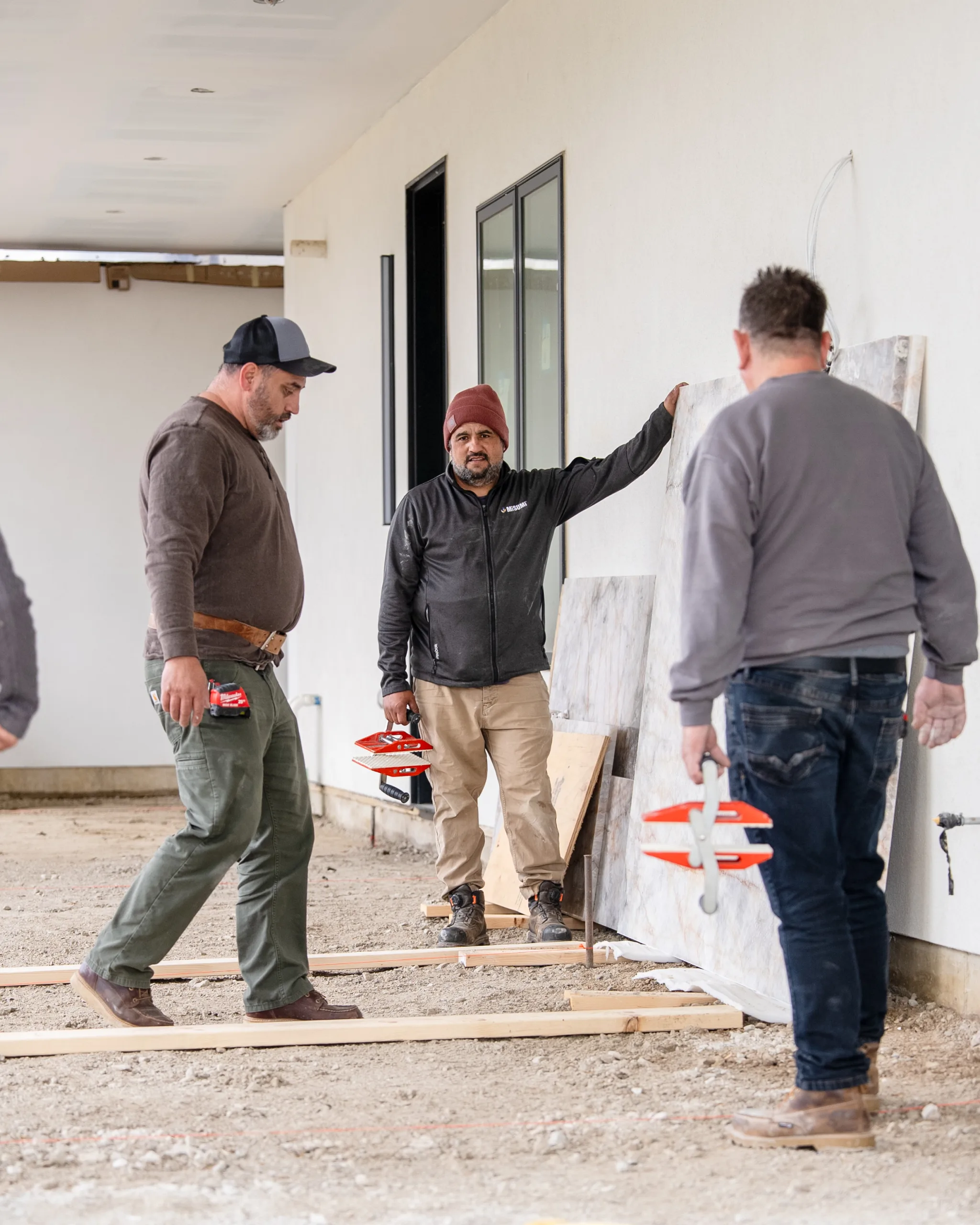 Three installers with slab-lifting clamps preparing marble panels at a home construction site