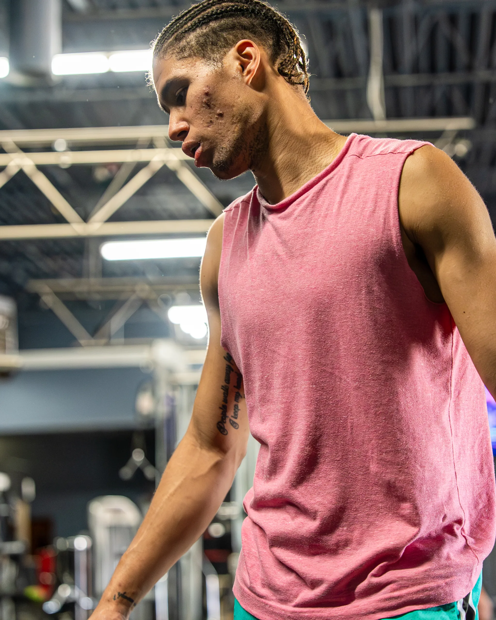 Athlete with braided hair in a pink sleeveless shirt training in a gym with steel trusses overhead