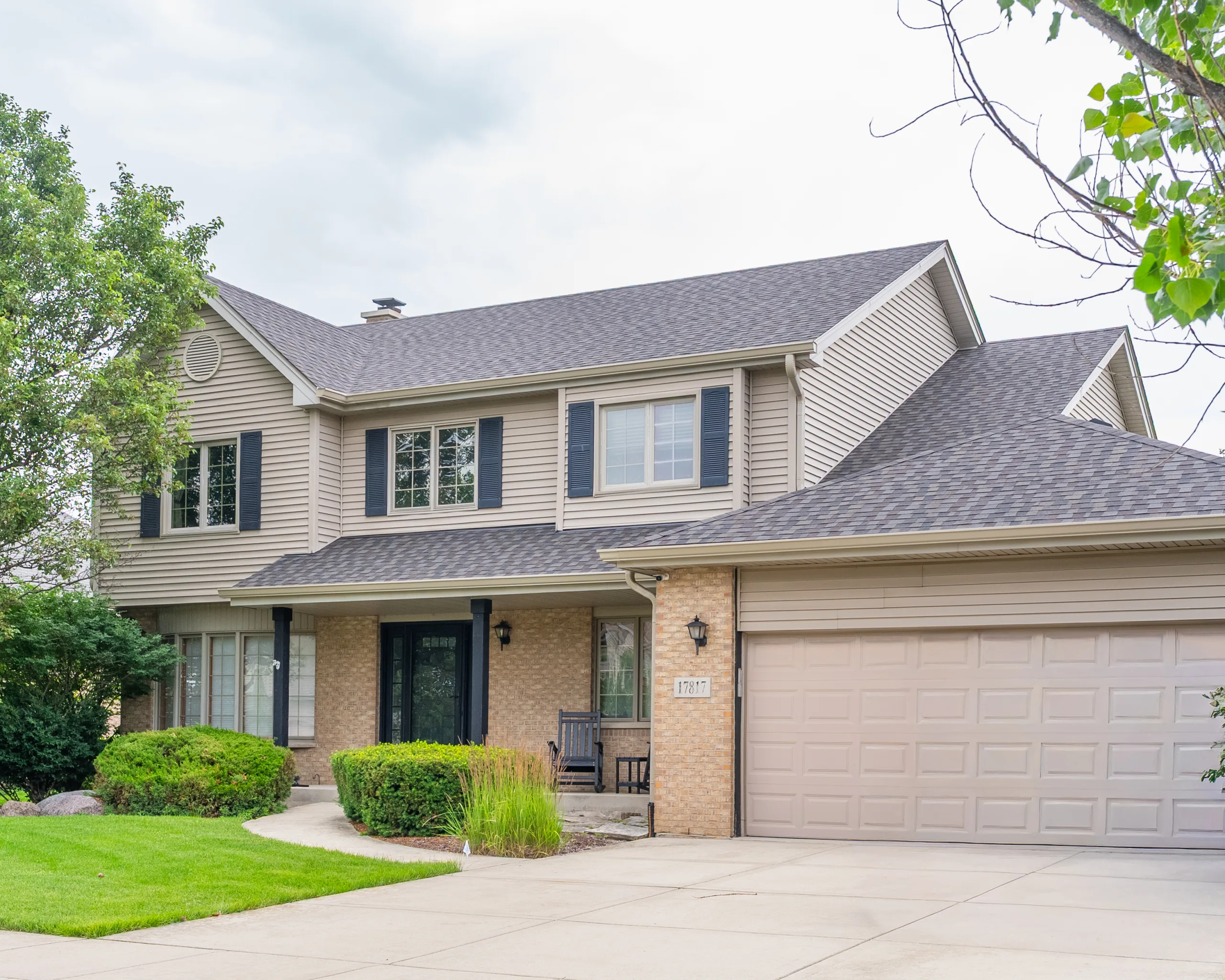 Angled view of a two-story home with gray architectural shingle roof, tan siding, and attached two-car garage