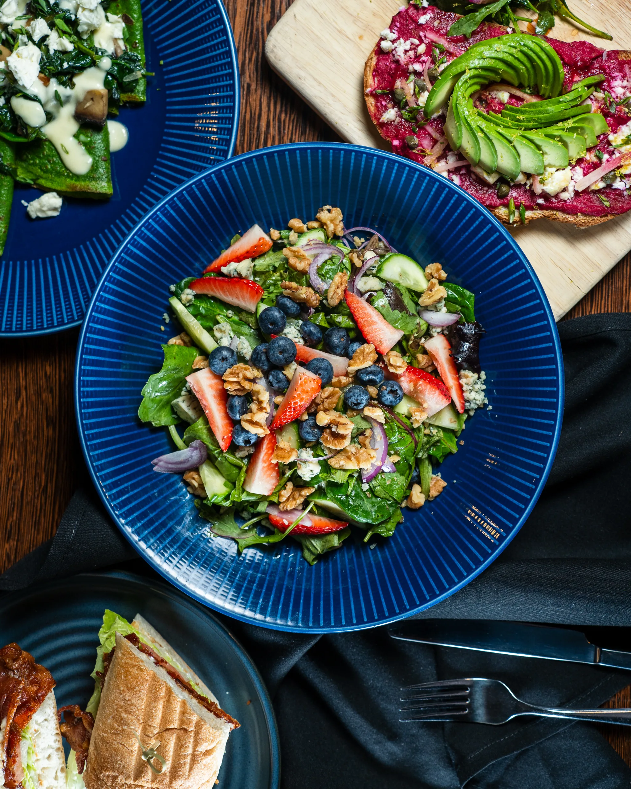 Mixed greens salad with strawberries, blueberries, walnuts, and blue cheese on a blue plate among brunch dishes