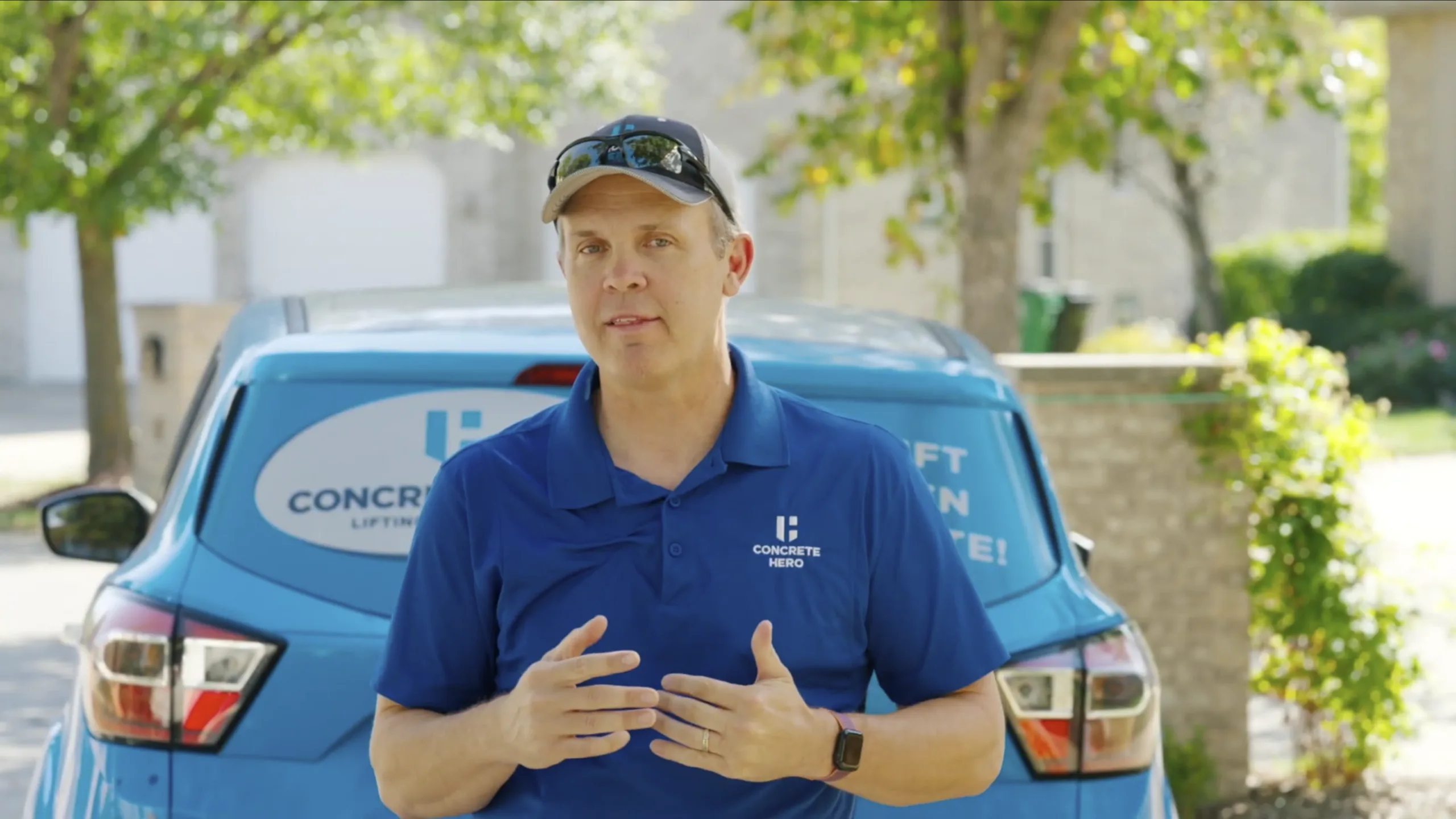 Concrete Hero owner in a blue branded polo speaking in front of a company SUV in a residential driveway