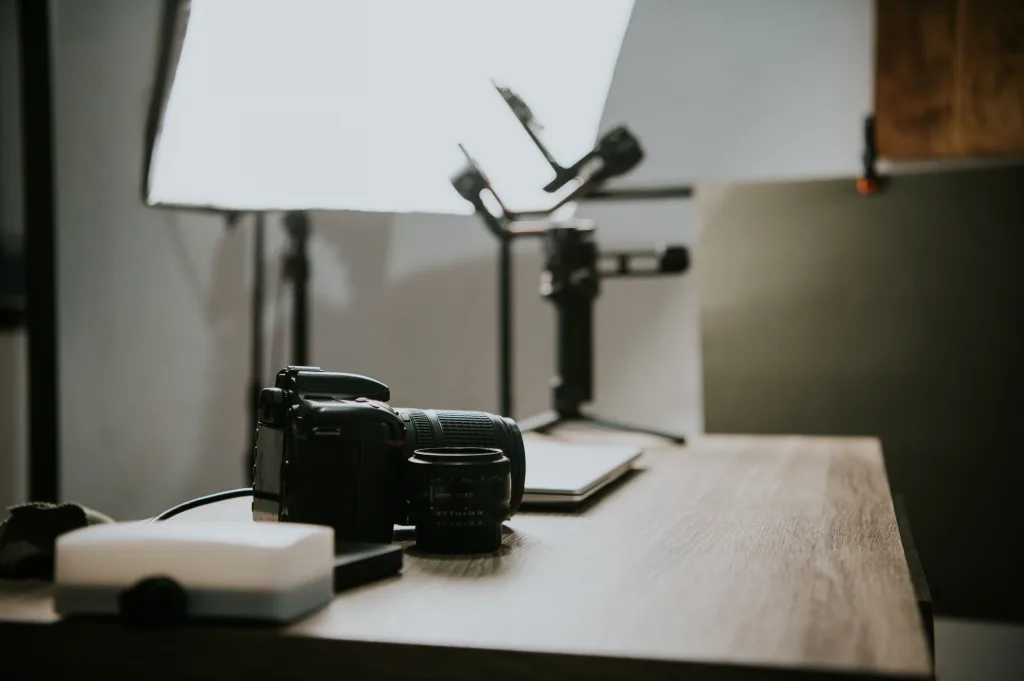 DSLR camera and lens on a wooden desk beside a softbox light and gimbal in a studio