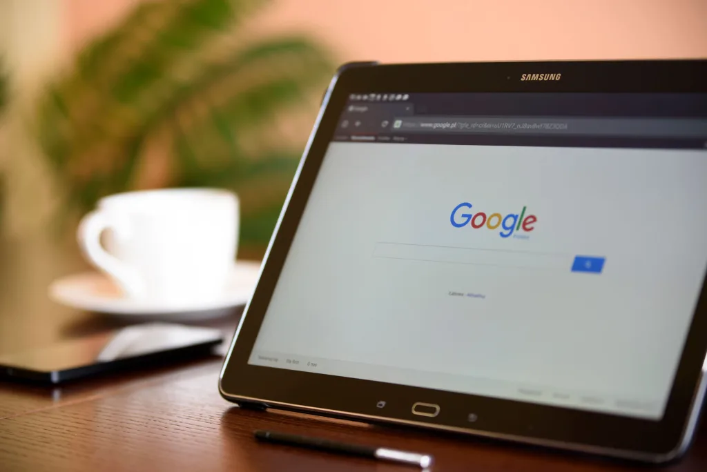 Samsung tablet propped on a desk displaying the Google search page, with a coffee cup and stylus nearby
