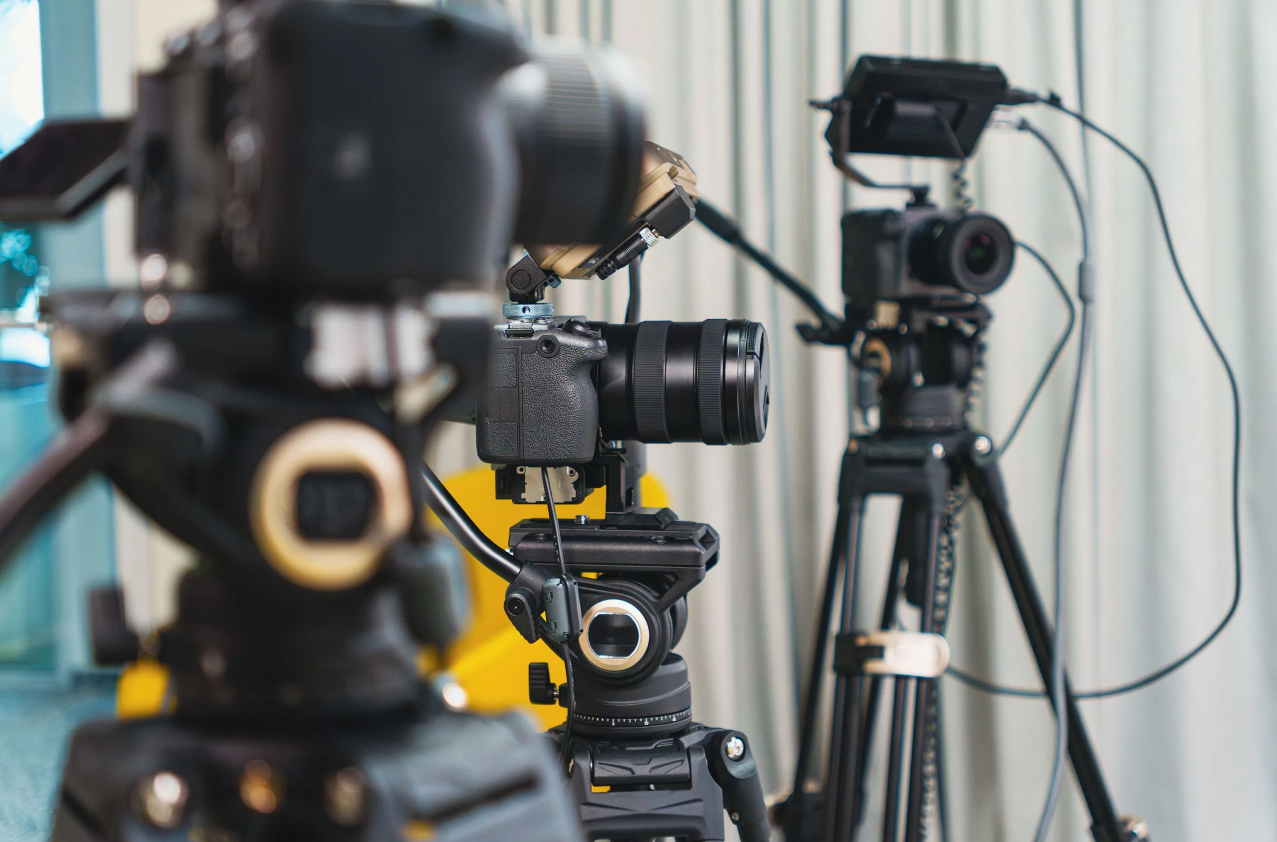 Video cameras on tripods lined up in front of gray curtains for a studio shoot
