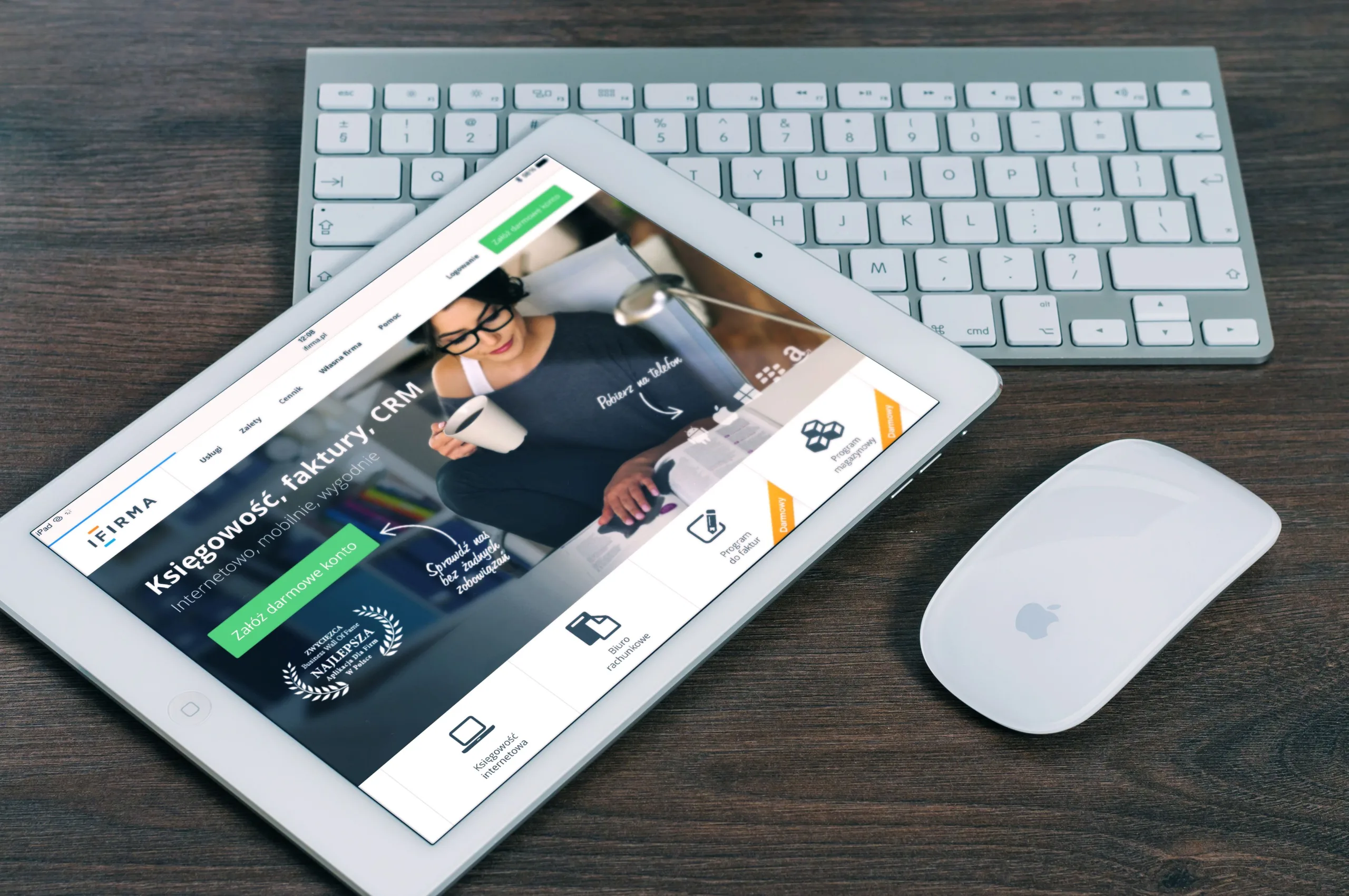 iPad displaying a business website homepage, resting on a white keyboard beside an Apple mouse on a dark wood desk
