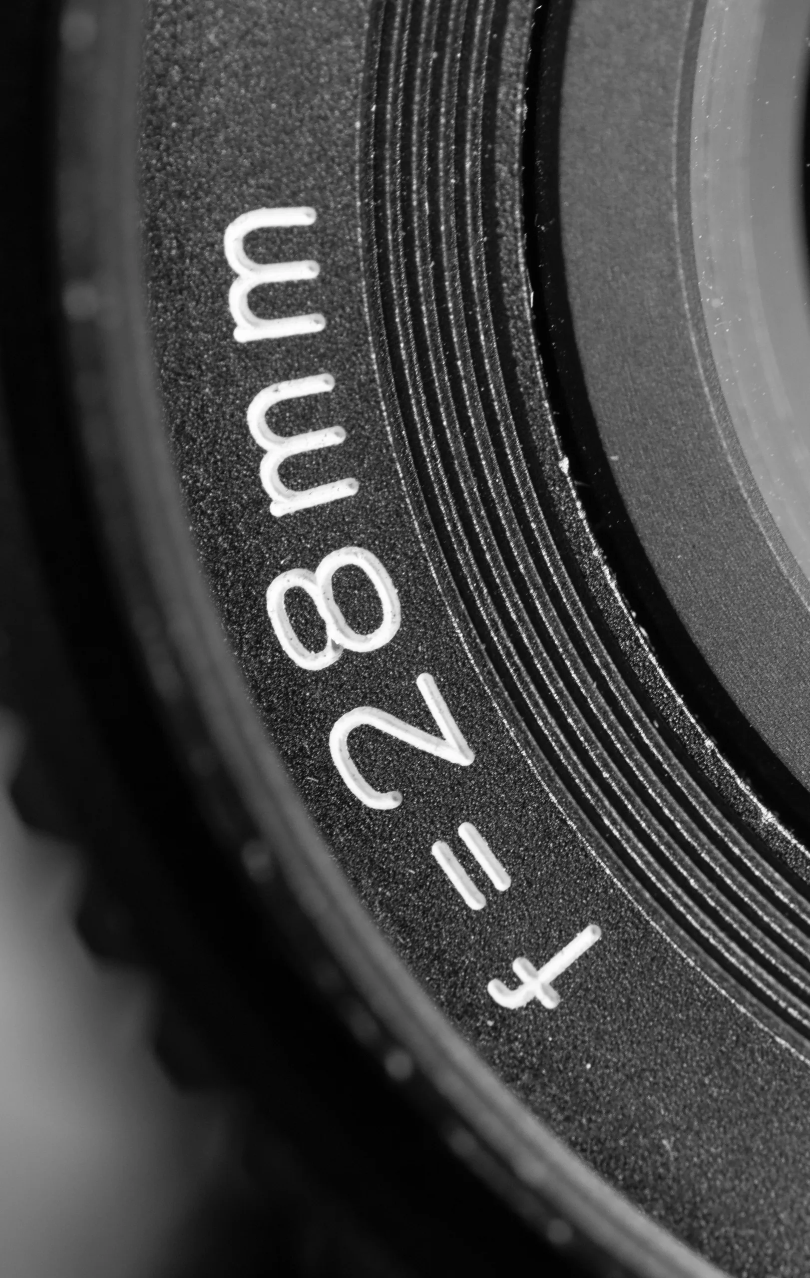 Black and white macro of a camera lens barrel engraved with the f=28mm focal length marking