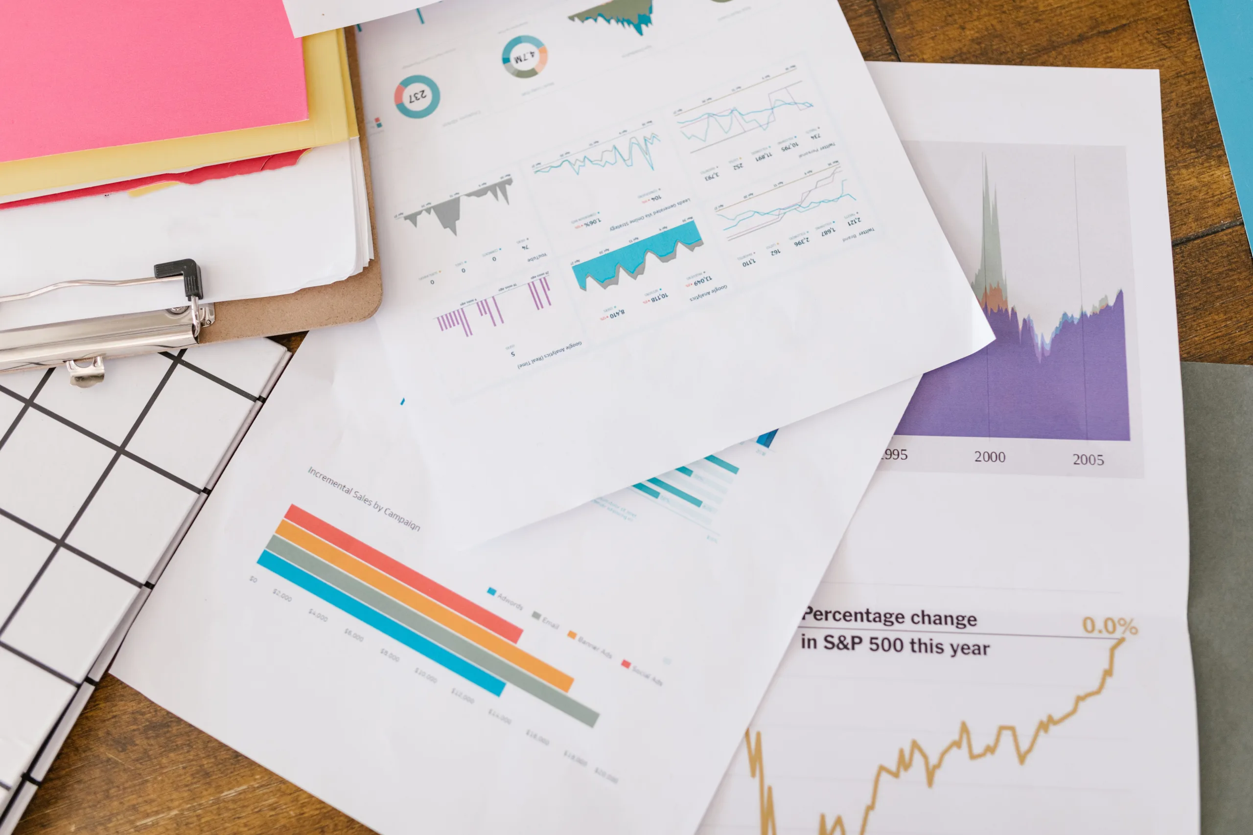 Printed analytics reports spread across a wooden desk, including campaign sales and S&P 500 charts